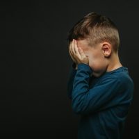 Kind dat zich probeert weg te steken achter zijn handjes op een zwarte achtergrond