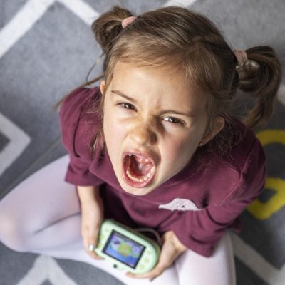 Boos kind op speeltapijt met videospelletje in de hand